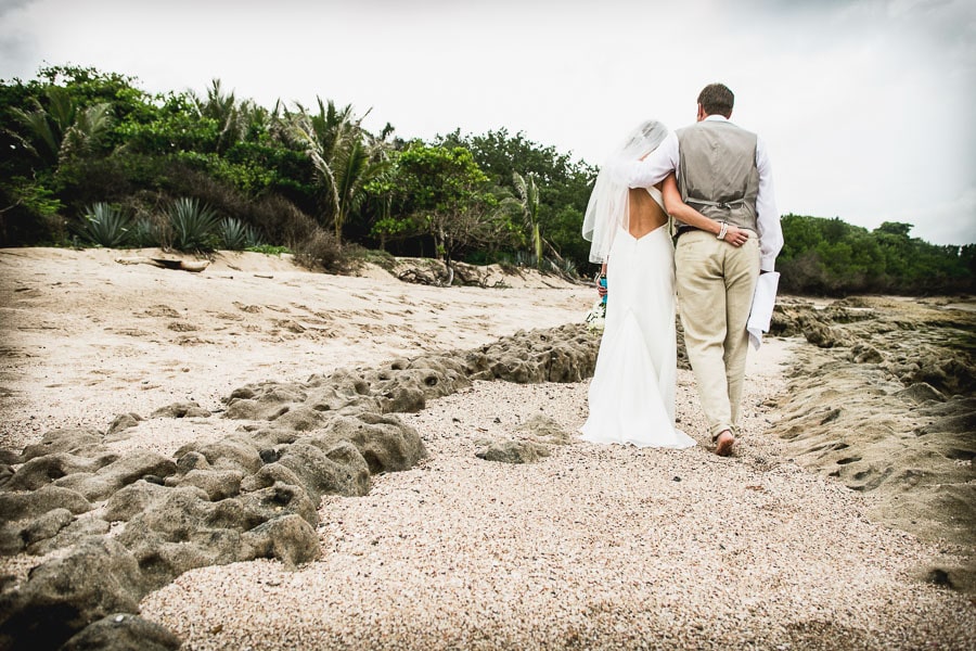 Bride and groom walk on beach.