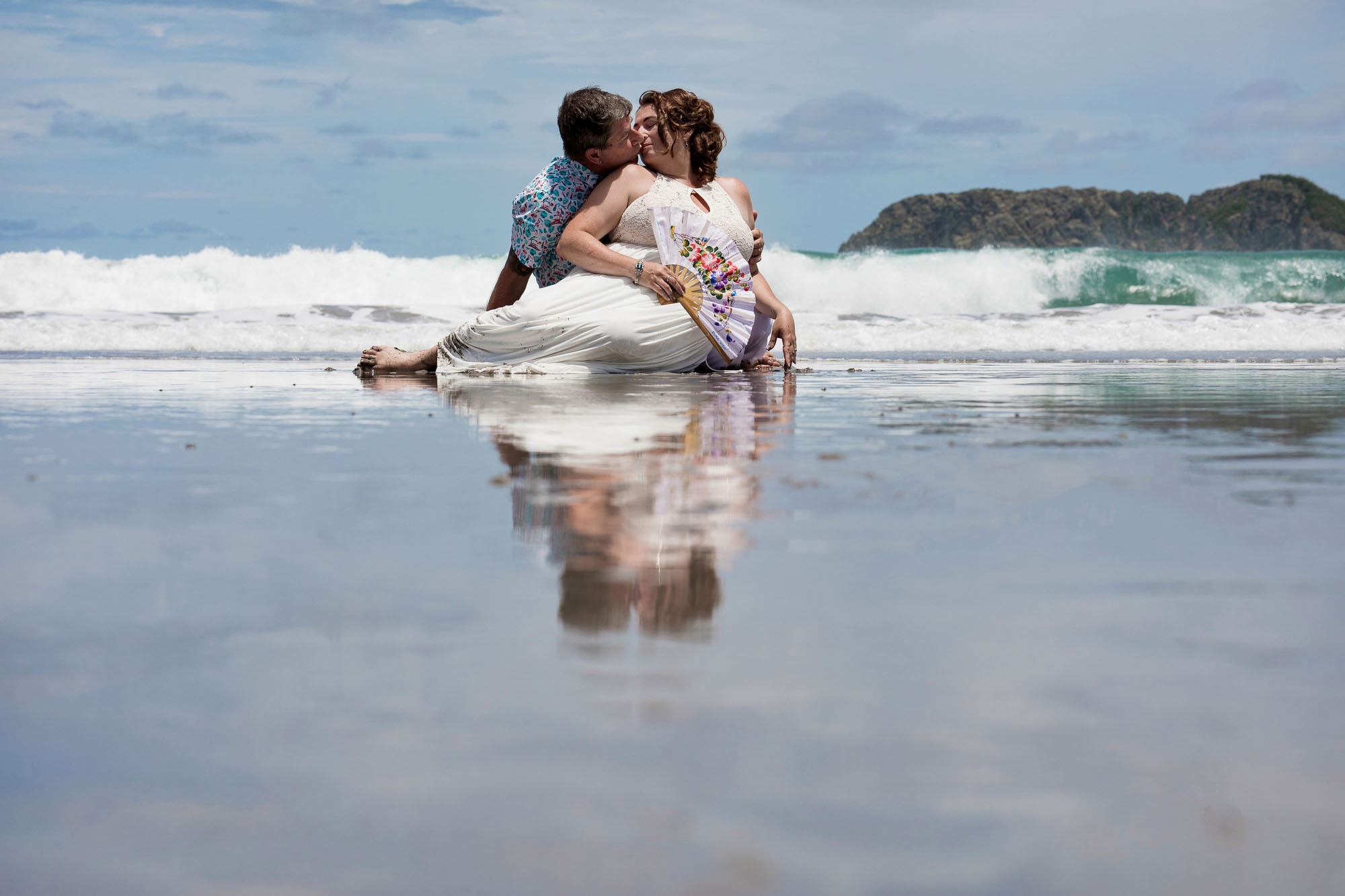 Bride and groom share a kiss at the water's edge on the beach