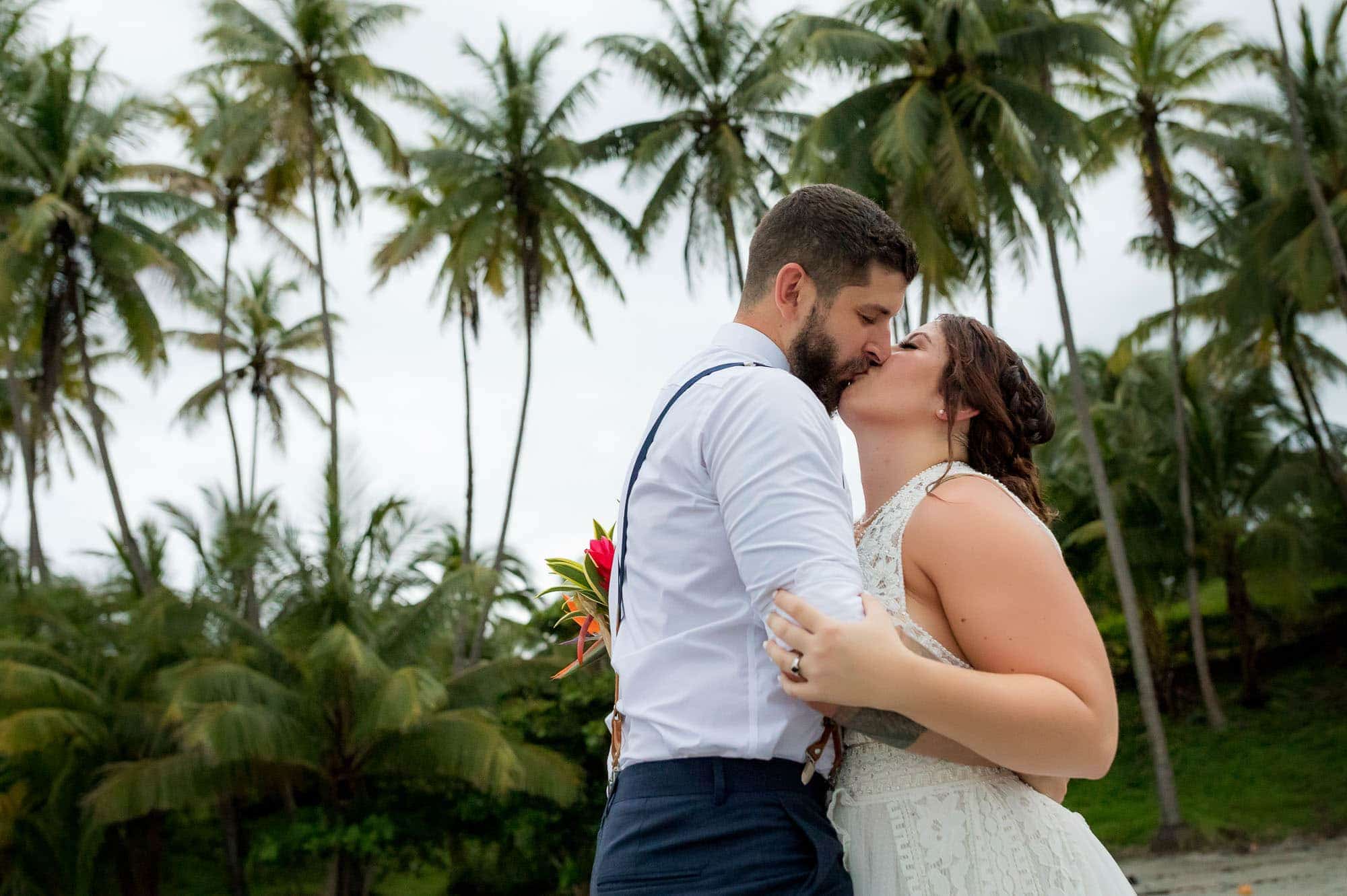 bride and groom kissing on the beach with palm trees in the background
