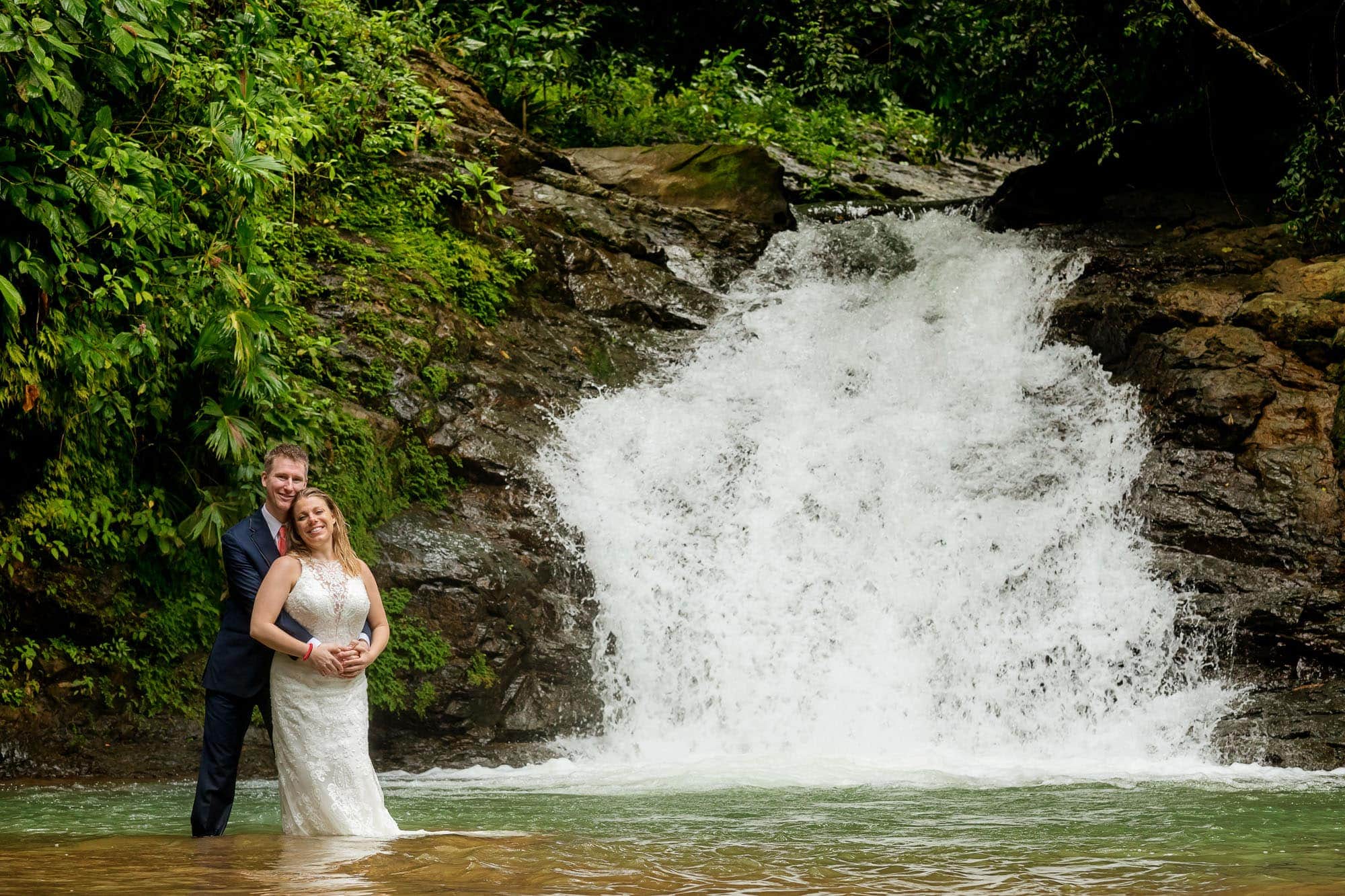 Bride and groom posing off the beaten path in Costa Rica at the base of a waterfall